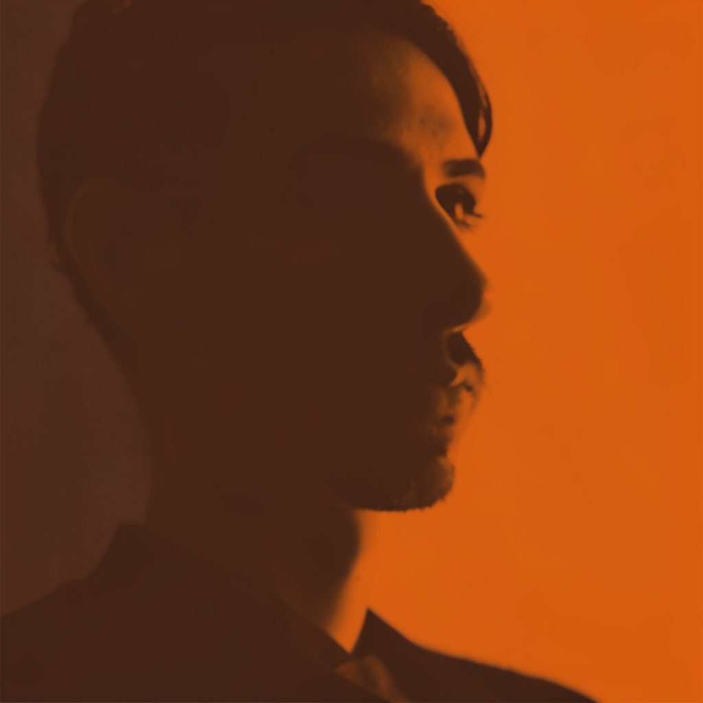 Cropped duotone scene of cast members gathered on set, deep blue shadows against warm amber light